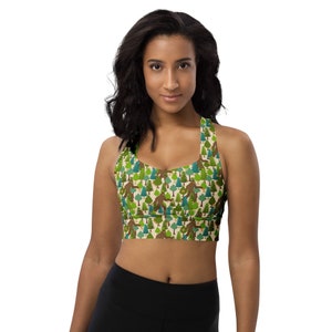 May include: A black and green sports bra with a repeating pattern of a Bigfoot figure walking through a forest of green trees. The bra has a racerback style.