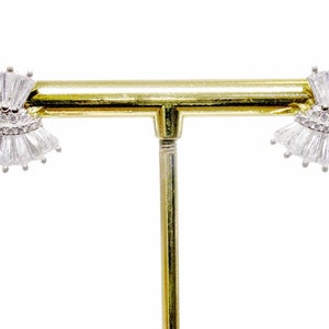 May include: A pair of silver earrings with a fan-shaped design featuring clear cubic zirconia stones. The earrings are displayed on a gold stand.