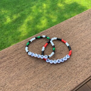 Puede incluir: Dos pulseras de cuentas con los nombres "Yelena" y "Natasha" deletreados en cuentas negras. Las cuentas son blancas, negras, rojas y verdes.