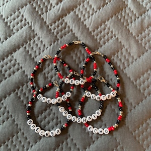 May include: Five beaded bracelets with black and red beads and white letter beads spelling out the words "Wrecker", "Tech", "Hunter", "Crosshair", and "Echo".
