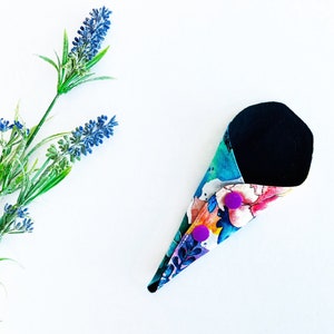 May include: A reusable menstrual pad with a black fabric lining and a colorful floral print. The pad has two purple buttons.