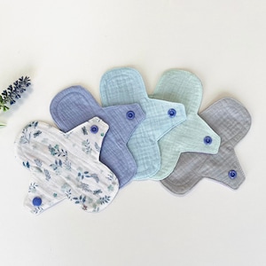 May include: Four reusable cloth menstrual pads in various shades of blue and green. One pad has a white background with a blue floral pattern.