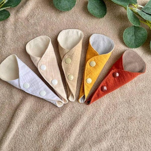 May include: Five reusable cloth pads in different colors and fabrics, including beige, white, yellow, orange, and brown. Each pad has a button closure.