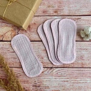 Op de afbeelding: Vijf roze herbruikbare menstruatiedoekjes op een houten oppervlak. De doekjes zijn gemaakt van een zacht, absorberend materiaal en zijn ontworpen om comfortabel en discreet te zijn.