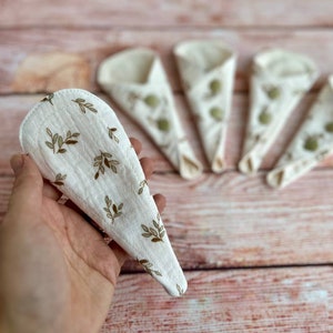 May include: Five white reusable makeup remover pads with a brown leaf pattern. The pads are folded in half and are arranged in a semi-circle on a wooden surface.