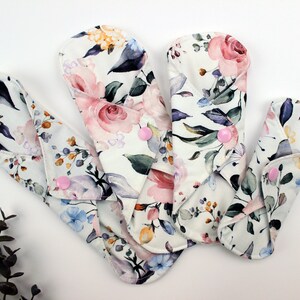 May include: Four reusable cloth menstrual pads with a floral print in shades of pink, purple, blue, and green. The pads have pink poppers.