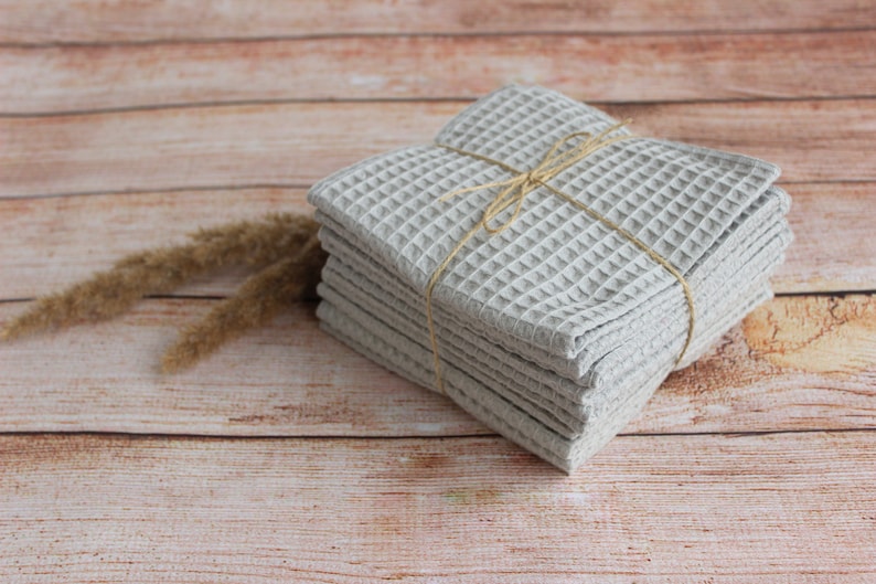 May include: A stack of gray waffle weave kitchen towels tied together with twine. The towels are on a wooden surface.