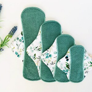 May include: Four reusable cloth menstrual pads in different sizes. The pads are green on one side and have a white floral print on the other side.