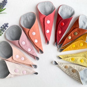 May include: A set of ten reusable menstrual pads in a rainbow of colors, folded and arranged in a circle. Each pad has a gray fabric lining and a button closure.