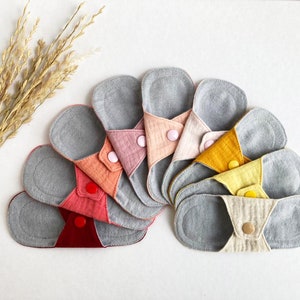 May include: A set of 10 reusable cloth menstrual pads in various colors, including gray, pink, orange, yellow, and red. The pads are made of soft, absorbent fabric and have a snap closure.