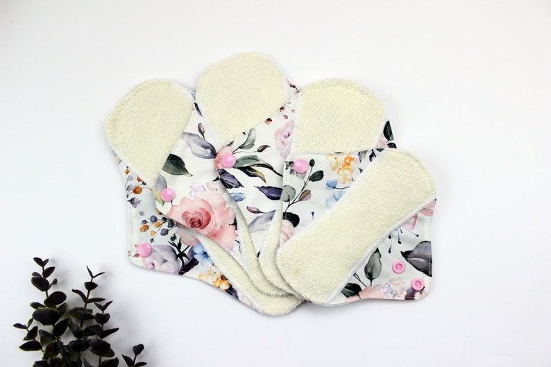 May include: Four reusable cloth menstrual pads with a floral print and white terry cloth backing. The pads have pink snaps.