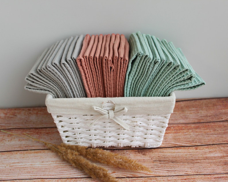 May include: A white wicker basket filled with stacks of kitchen towels in gray, peach, and green.