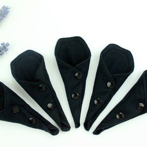 May include: Five black reusable cloth menstrual pads with snap closures. The pads are folded in half and arranged in a semi-circle.