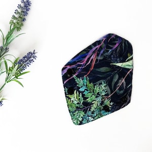 May include: A dark blue reusable menstrual pad with a floral print featuring green, purple, and pink watercolor leaves. The pad has black snaps on the sides.