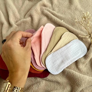 May include: A set of seven reusable cloth pads in various colors, including pink, beige, and white. The pads are made of soft, absorbent fabric and are designed for menstrual hygiene.