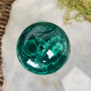 Pode incluir: Uma esfera de malaquita verde com padrões e redemoinhos intrincados. A esfera é polida e tem um acabamento brilhante.