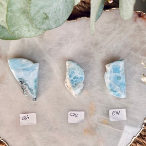 May include: Three blue and white polished stones with a marbled pattern. The stones are labeled with the numbers "B33", "C24", and "E24".
