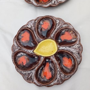 May include: A brown and white ceramic oyster plate with six individual indentations for serving oysters. The plate has a yellow center indentation for serving sauce or butter.