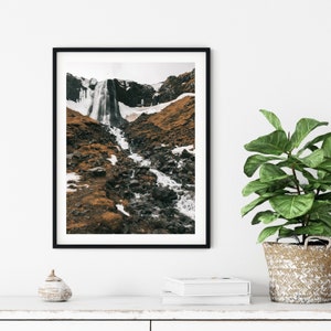 May include: A black and white photograph of a waterfall cascading down a rocky hillside. The waterfall is surrounded by brown and green vegetation.