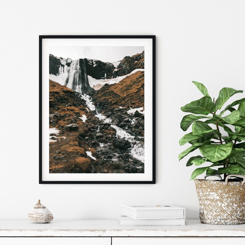 May include: A black and white photograph of a waterfall cascading down a rocky hillside. The waterfall is surrounded by brown and green vegetation.