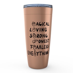 K&ouml;nnte beinhalten: Ein ros&eacute;goldener Becher mit einem schwarzen Design, auf dem "MAGICAL LOVING STRONG HONEST FEARLESS EVERYTHING" mit Geb&auml;rdensprachsymbolen f&uuml;r jedes Wort steht.