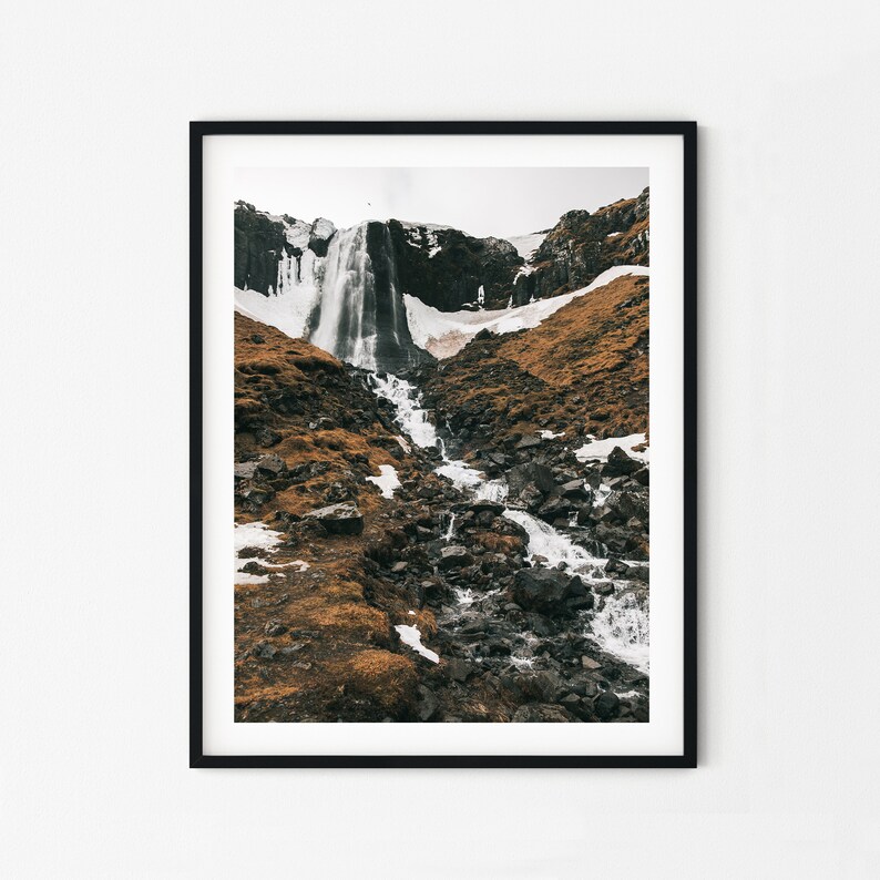 May include: A black and white photograph of a waterfall cascading down a rocky mountainside. The waterfall is partially frozen, and the surrounding landscape is covered in snow and ice.