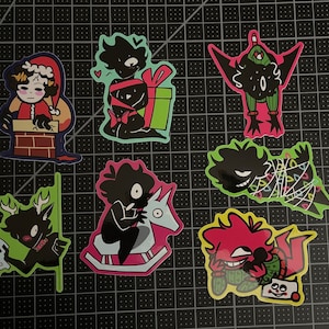 以下が含まれることがあります： クリスマスをテーマにした8枚のステッカーセット。白黒の漫画キャラクターが様々な休日のアクティビティをしています。ステッカーは光沢のある仕上げの白い紙に印刷されています。