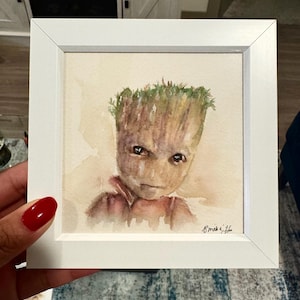 May include: A square white frame containing a watercolor painting of a tree-like creature with brown bark-textured skin, large dark eyes, and green foliage on its head. The artwork features a signature in the bottom right corner and a light background.