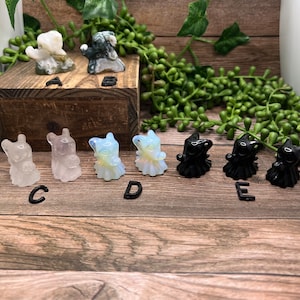 May include: Seven small carved crystal figurines, including two white, two light blue, and three black. The figurines are arranged in a row on a wooden surface.
