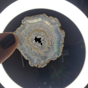 May include: A white agate slice with a natural hole in the centre. The agate has a translucent, milky white colour with a hint of brown around the edges.