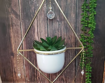 May include: A gold geometric planter with a white ceramic pot and a succulent plant. The planter has a crystal hanging from the top and gold chains hanging from the bottom.