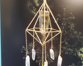 May include: A gold-coloured crystal suncatcher with a geometric design. It features a central clear crystal within a gold wire frame, with clear crystal pendants suspended from gold chains. The suncatcher hangs from a gold chain.