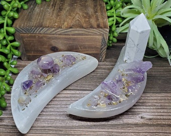 May include: Two white selenite crescent moon shaped dishes with amethyst crystals and gold flecks. One dish has a small amethyst mushroom on top. The other dish has a white selenite tower.