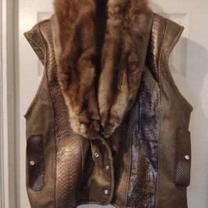 May include: A brown leather waistcoat with a large fur collar and a snakeskin pattern on the front. The waistcoat has a button fastening and two pockets on the sides.
