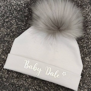 May include: White baby hat with a fluffy pom pom and the text "Baby Dale" embroidered in silver.