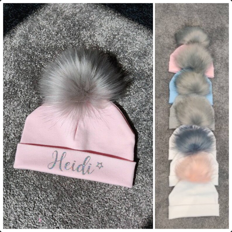 May include: Pink knitted baby hat with a fluffy gray pom pom and the name "Heidi" embroidered on the front.
