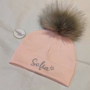 May include: Pink knit beanie with a fluffy gray pom pom and the name "Sofia" in sparkly silver letters with a star.