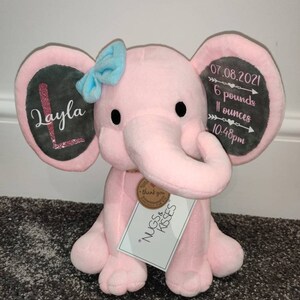 May include: Pink plush elephant stuffed animal with a gray ear tag that says "Layla" and another gray ear tag that says "07.08.2021 6 pounds 11 ounces 10:48pm". The elephant is holding a small brown tag that says "Thank you for the NUGS & KISSES".
