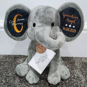 Op de afbeelding: Een grijze pluche olifant met geborduurde details op de oren. Op &eacute;&eacute;n oor staat "Cian Jamie Murray" en op het andere "Guardian Angel" met een datum. Een label leest "Nugs & Kisses".