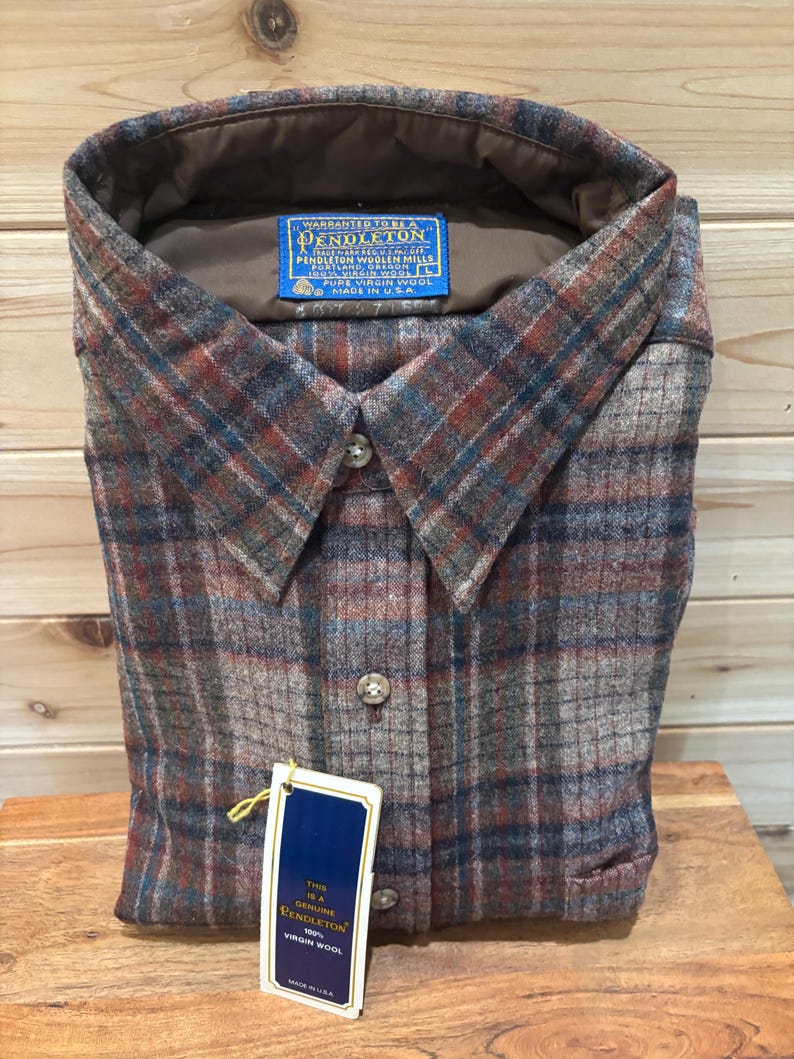 May include: A folded Pendleton button-down shirt in a plaid pattern of brown, red, and blue. The shirt has a collar and buttons down the front. A tag reads "Genuine Pendleton 100% Virgin Wool" and "Made in USA."