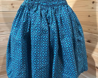 Könnte beinhalten: Ein türkisfarbener und marineblauer Rock mit floralem Muster. Der Rock hat einen gerafften Bund und einen vollen, gerafften Rock. Der Stoff ist ein leuchtendes Türkis mit einem sich wiederholenden marineblauen Blumendesign. Der Rock wird auf einer Schaufensterpuppe präsentiert.