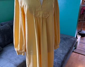 May include: A long, yellow, cotton dress with a V-neck and long sleeves. The dress has a gathered waist and a slightly flared skirt.