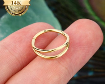May include: Gold double hoop nose ring with a 14K marking. The ring is shown on a finger.