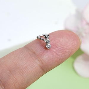 May include: A silver nose ring with three clear cubic zirconia stones set in a vertical line.
