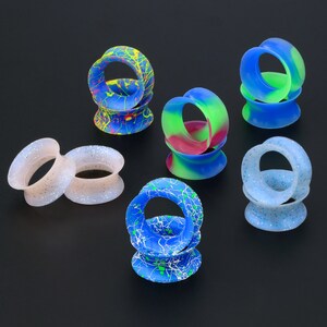 May include: Assortment of colorful silicone ear gauges in various patterns, including white glitter, blue and green swirl, blue with white streaks, and blue with green and yellow paint splatters.
