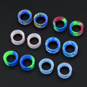 May include: Assortment of colorful silicone ear gauges in various sizes and patterns. The gauges feature a variety of colors, including blue, green, red, and white.