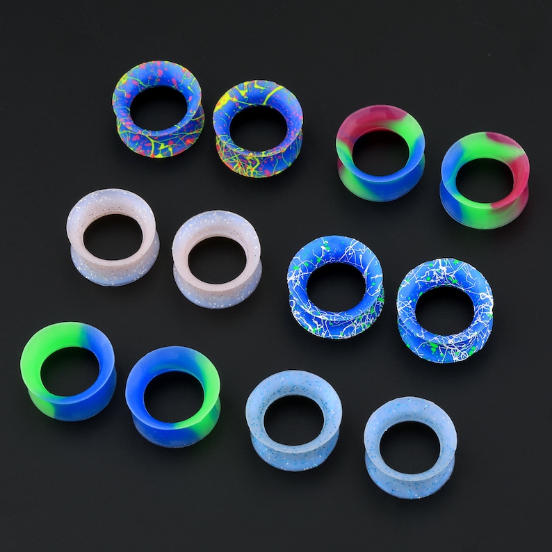 May include: Assortment of colorful silicone ear gauges in various sizes and patterns. The gauges feature a variety of colors, including blue, green, red, and white.