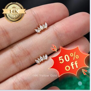 May include: Two 14K yellow gold stud earrings, each featuring a crown-like design set with multiple clear marquise and round-cut cubic zirconia stones. The jewelry is labeled 14K and 14K Yellow Gold, with a 50% off graphic overlay.