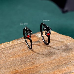 May include: Two black rings with a red gemstone in the center. The rings are 8mm wide and are labeled 22G and 20G.