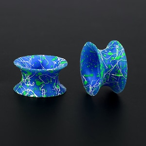 May include: Two blue and green ear gauges with a white splatter paint design. The gauges are made of a smooth, flexible material.
